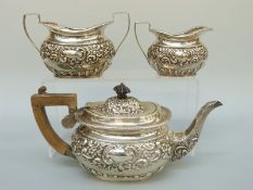 An Edward VII hallmarked silver three piece tea set with repoussé decoration and vacant cartouches,