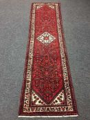 A North West Persian runner on red ground with central cream medallion, with vine borders,