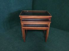 A nest of three teak glass topped tables