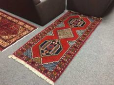 A fringed Persian rug on red ground with central medallion design 190 cm x 90 cm