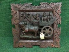 A heavily carved Eastern wall panel depicting three figures on a cart