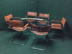 A contemporary glass topped dining table with a set of six tan leather sling chairs on tubular