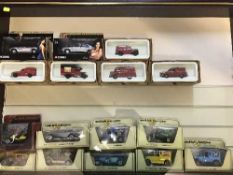 A glass door wall mounted display case containing sixteen boxed die-cast vehicles including Corgi