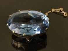 A yellow metal brooch set with a large blue stone