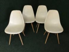 A set of four cream plastic bucket chairs on wooden legs