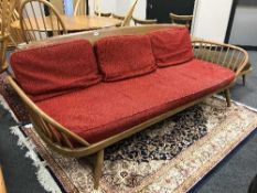An Ercol elm day bed with red upholstered cushions
