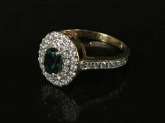 A diamond cluster ring with green central stone,