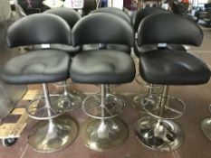 A set of six black leather swivel bar chairs on chrome bases
