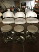 A set of three white leather swivel bar chairs on chrome bases and three swivel bar stools