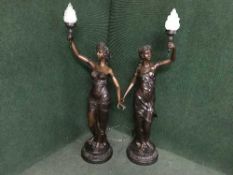 A pair of patinated spelter floor lamps modelled as classical figures bearing torches, with shades.