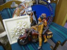 A decorative frameless mirror together with a relief plaque and a wooden motorcycle with rider and