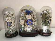 Three antique glass domes on bases containing dried flowers
