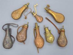Eight assorted copper and brass powder flasks with embossed decoration.