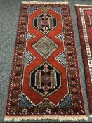 A geometric designed rug on red ground 195 cm x 91 cm