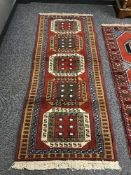 A geometric designed rug on red ground 210 cm x 80 cm