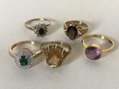 A collection of five gold rings including one set with a green stone and diamonds