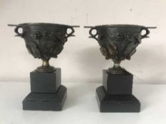 A pair of bronze urns on marble plinths with embossed leaf and vine decoration (2)