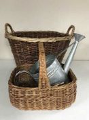 A large wicker log basket containing a wicker hand basket, aluminium watering can,