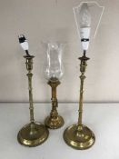 A 20th century brass rise and fall hurricane candlestick and a pair of converted brass lamps