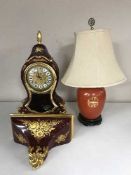 A decorative red and gilt bracket clock with wall bracket together with an Oriental style table