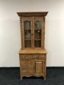 A stripped pine glazed bookcase with cupboards and drawers beneath