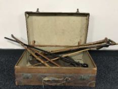 A vintage leather suitcase containing a quantity of walking sticks,