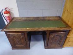 An antique oak and mahogany twin pedestal desk with carved panel doors inset green leather panel