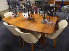 A shaped mid 20th century teak dining table and six cream vinyl upholstered chairs
