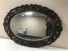 An oval mirror in a heavily carved oak frame