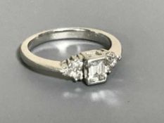 A platinum emerald cut diamond ring, with three round-cut diamonds to each shoulder, ring size K.