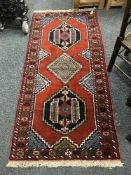 A fringed Persian geometric design rug on red ground 195 cm x 91 cm