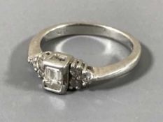 A platinum emerald cut diamond ring, with three round-cut diamonds to each shoulder, ring size K.