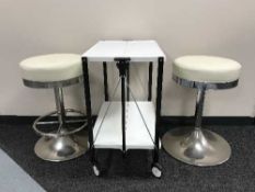 A folding metal two tier serving trolley together with two cream upholstered bar stools
