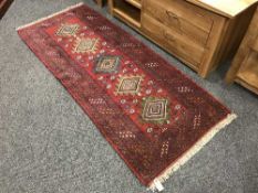 A fringed Persian geometric design rug on red ground 212 cm x 84 cm