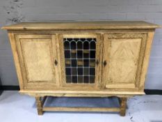 A blonde oak triple door sideboard with leaded glass panel