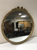 A gilt framed circular mirror with ornate bow topped frame