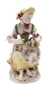 A Bow figure of a girl grape seller: emblematic of Autumn, seated barefoot and wearing a yellow hat,