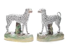 A pair of Staffordshire pottery Dalmatians: each standing before a stump in alert posture with