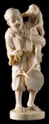 A Japanese carved ivory okimono: depicting a street musician holding a drum with a monkey on his