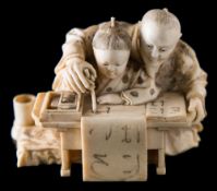 A Japanese carved ivory okimono: of a teacher and pupil at a table learning to write the alphabet,