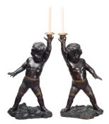 A pair of carved and stained wood standing figures of putti: each with a raised arm supporting a
