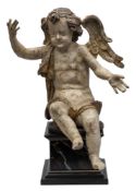 An Italian carved wood and polychrome decorated figure of a seated cherub: with outstretched arms