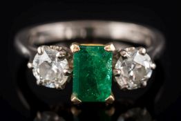 An emerald and diamond three-stone ring: the central rectangular emerald approximately 7.