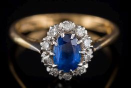 A sapphire and diamond oval cluster ring: the central, oval sapphire approximately 6.4mm long x 4.