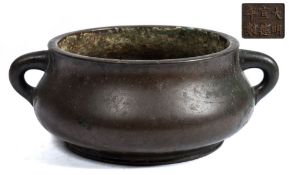 A Chinese bronze censer: of squat circular form with loop carrying handles to the sides,