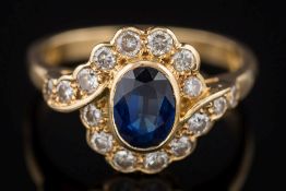 An 18ct gold, sapphire and diamond oval cluster ring: the central oval sapphire 7mm x 5mm,