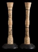 A pair of Japanese carved bone candlesticks: decorated with seated figures in traditional costume,