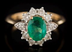 An emerald and diamond oval cluster ring: the oval emerald approximately 8.2mm long x 6.