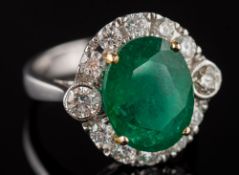 An emerald and diamond oval cluster ring: the central oval emerald approximately 12.5mm long x 9.
