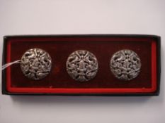 A set of three silver circular buttons:, pierced and decorated with scrolling foliage,